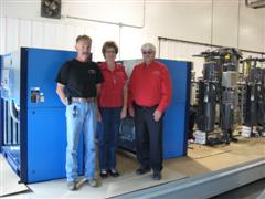 Staff standing beside a large blue industrial air compressor in a workshop.